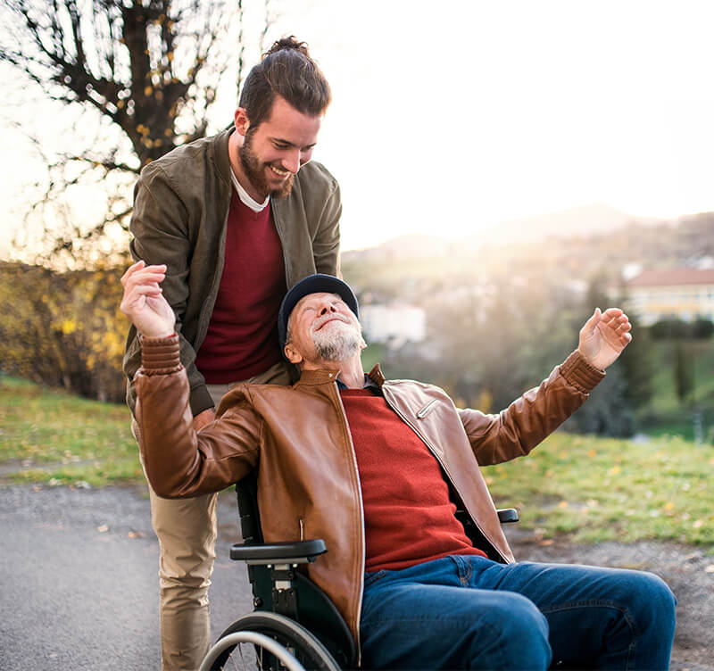 Young carer pushing smiling man in wheelchair